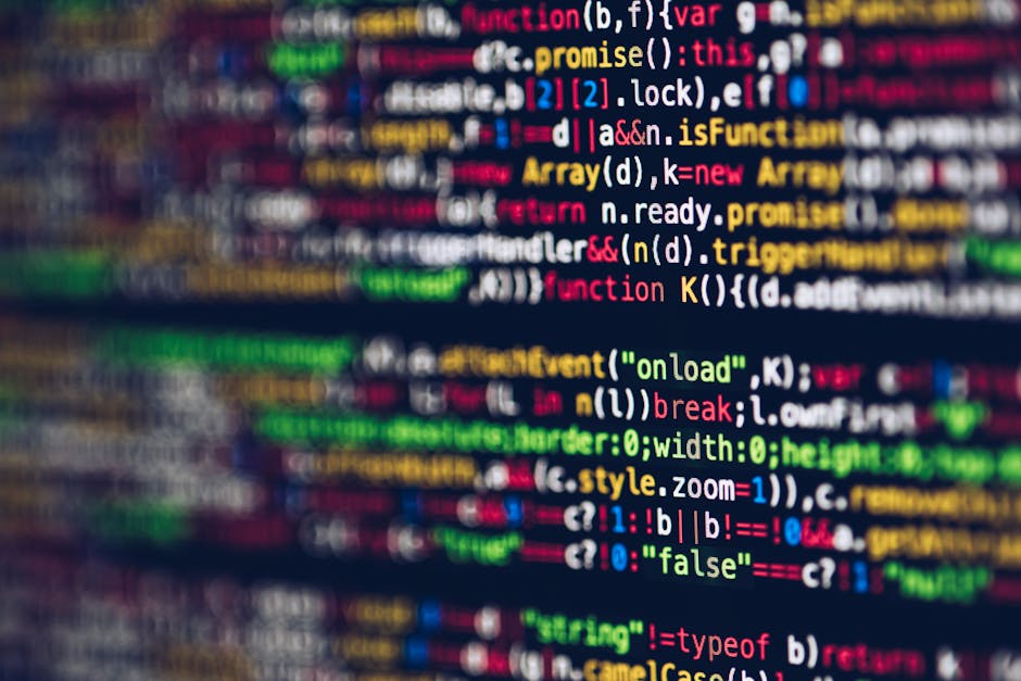 A close-up view of a person's hands typing on a laptop keyboard placed on a dark, reflective surface. The laptop screen displays lines of code with syntax highlighting in green, blue, and white text a